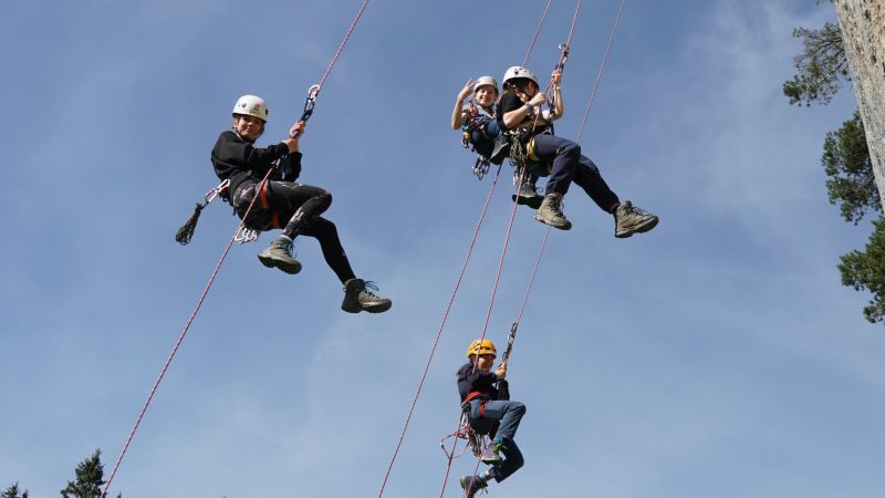 Drei Jugendliche seilen sich an einem Felsen ab