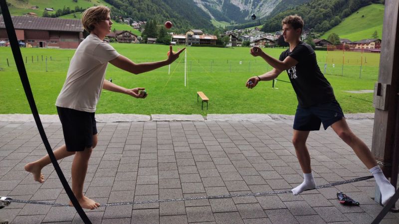 Zwei Jugendliche balancieren auf einer Slackline und Jonglieren