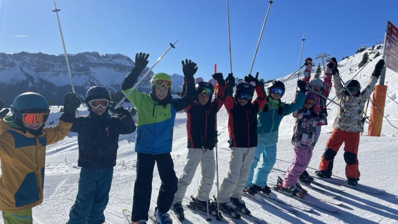 Acht Jugendliche mit Skiausrüstung stehen in einer Reihe auf der Skipiste