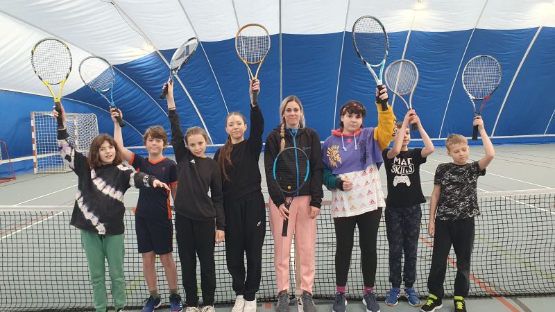 Jugendliche stehen in einer Reihe mit Tennisschläger in einer Tennishalle