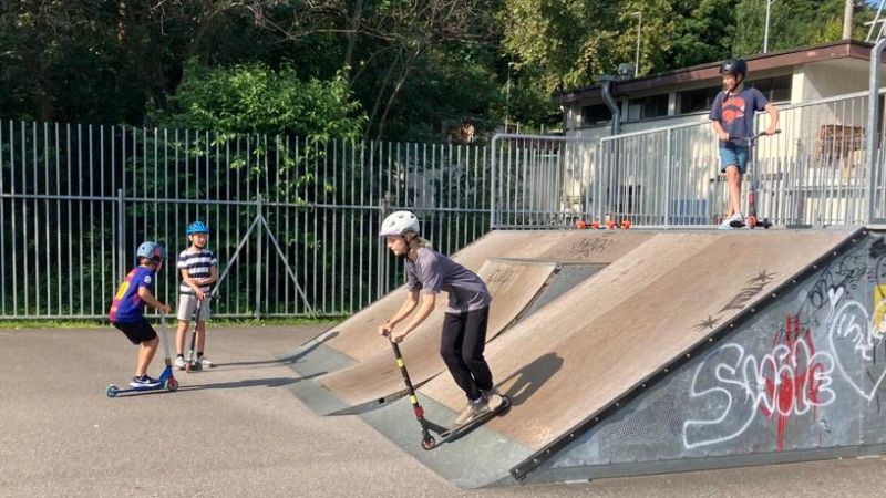 Jugendliche fahren mit Scooter auf Skate-Rampe 