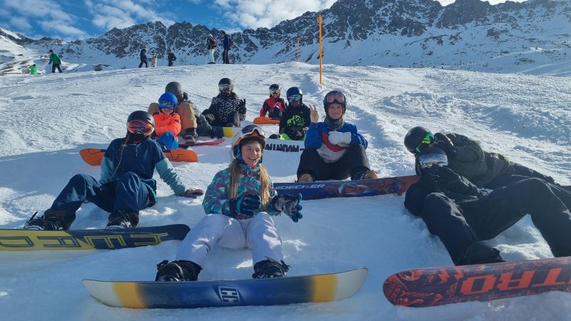 Jugendliche in Snowboardausrüstung sitzen auf der Piste